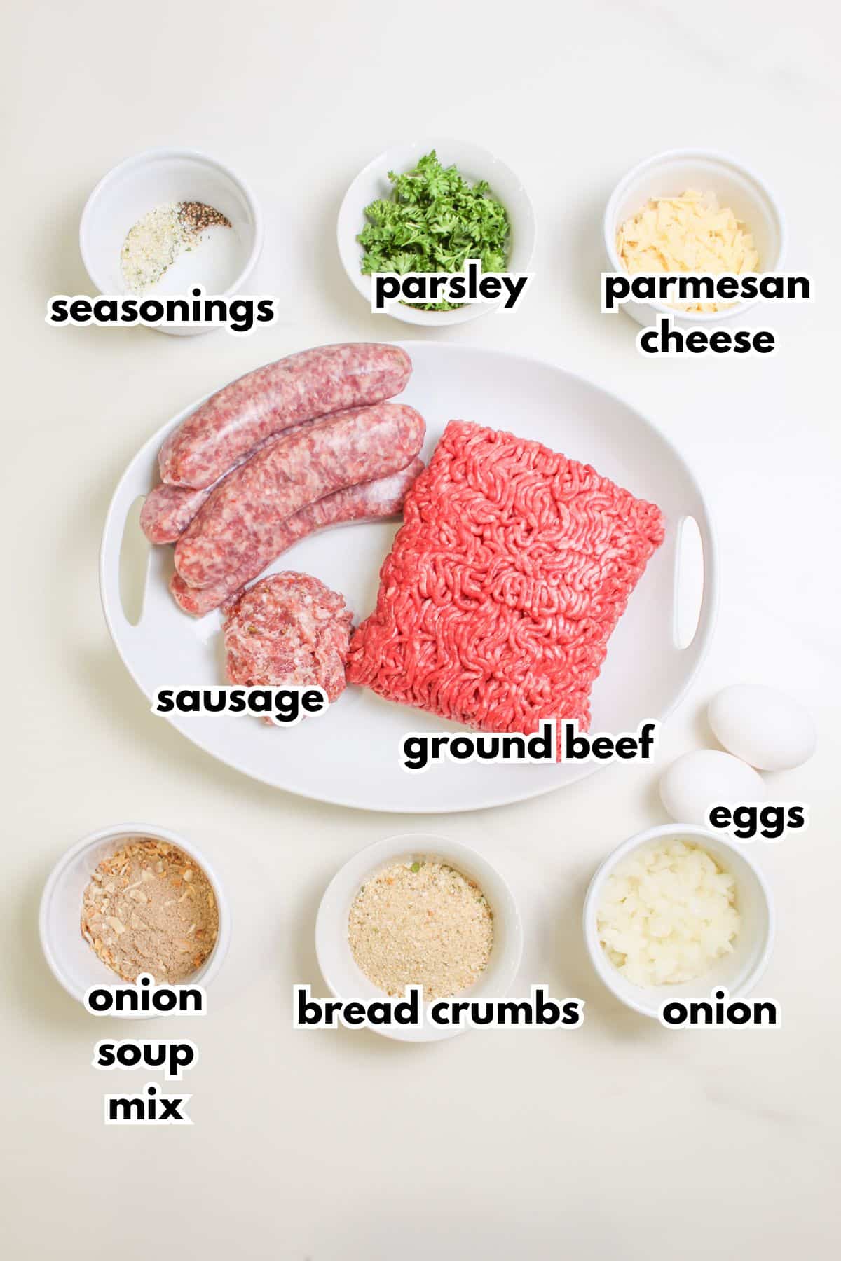 bowls of seasonings, parsley, parmesan cheese, sausage, ground beef, onion soup mix, bread crumbs, eggs, and onion on a counter.