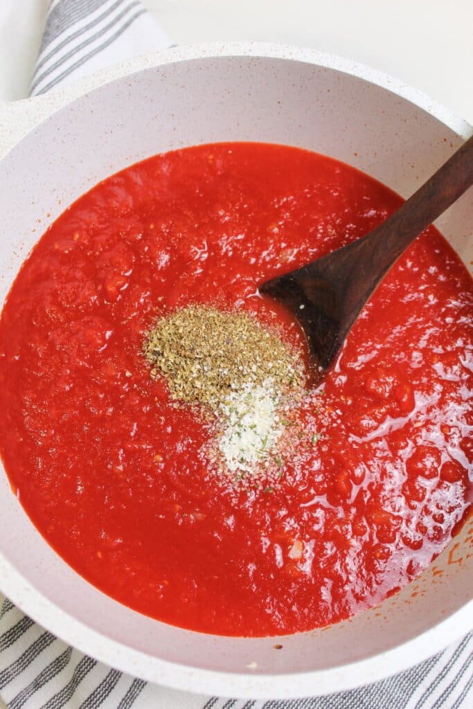seasonings being added to a pot of tomato sauce.