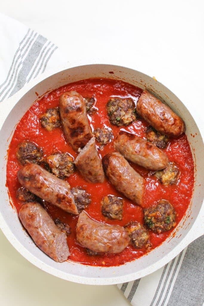 meatballs and sausage being added to a large pot.
