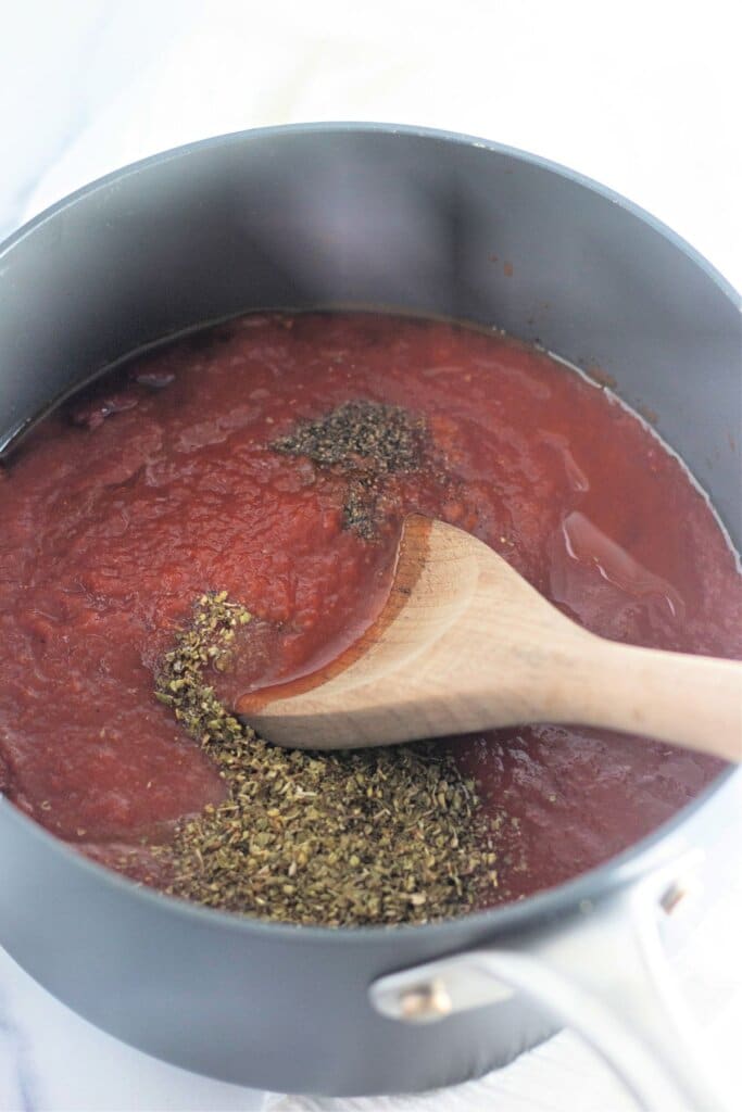 seasonings being added to a pot of tomato sauce.