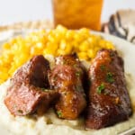 three honey bbq ribs on a plate with mashed potatoes and corn.