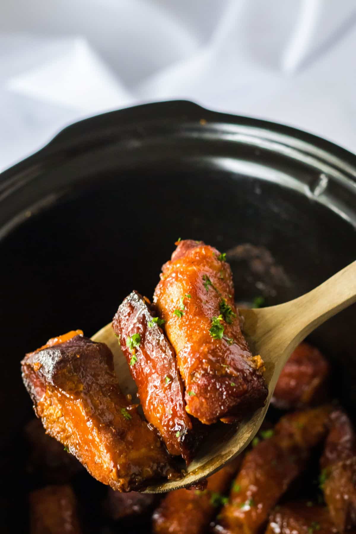 three country style ribs held on a wooden spoon in the air.