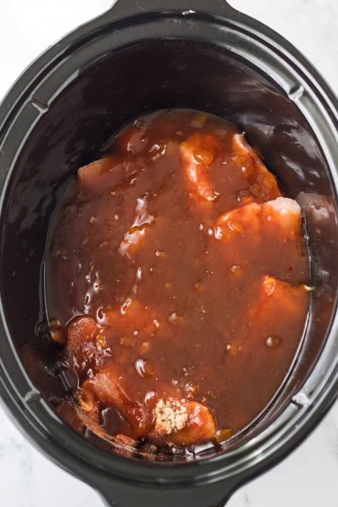 bbq sauce being poured on top of country ribs in a slow cooker.