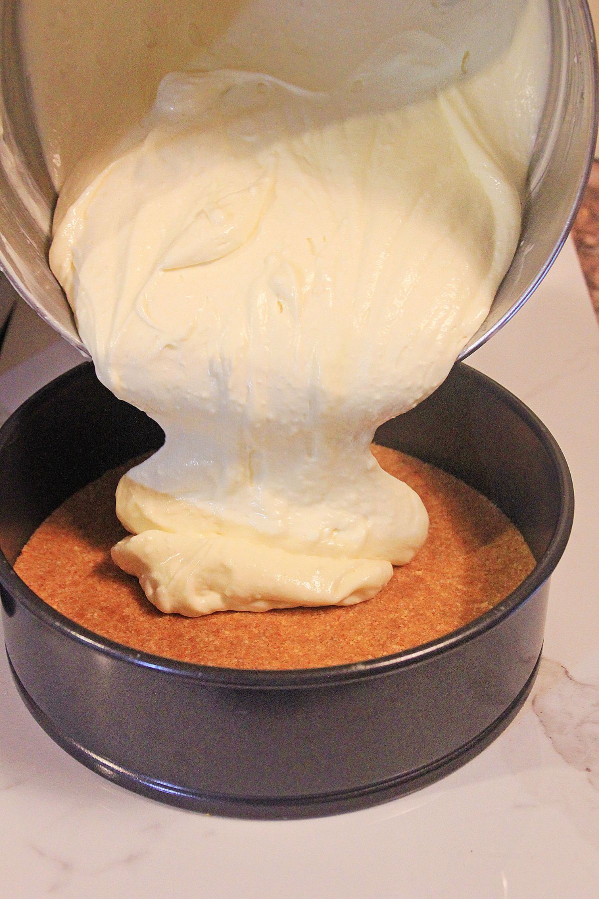 batter being poured on top of a crust in a springform pan.