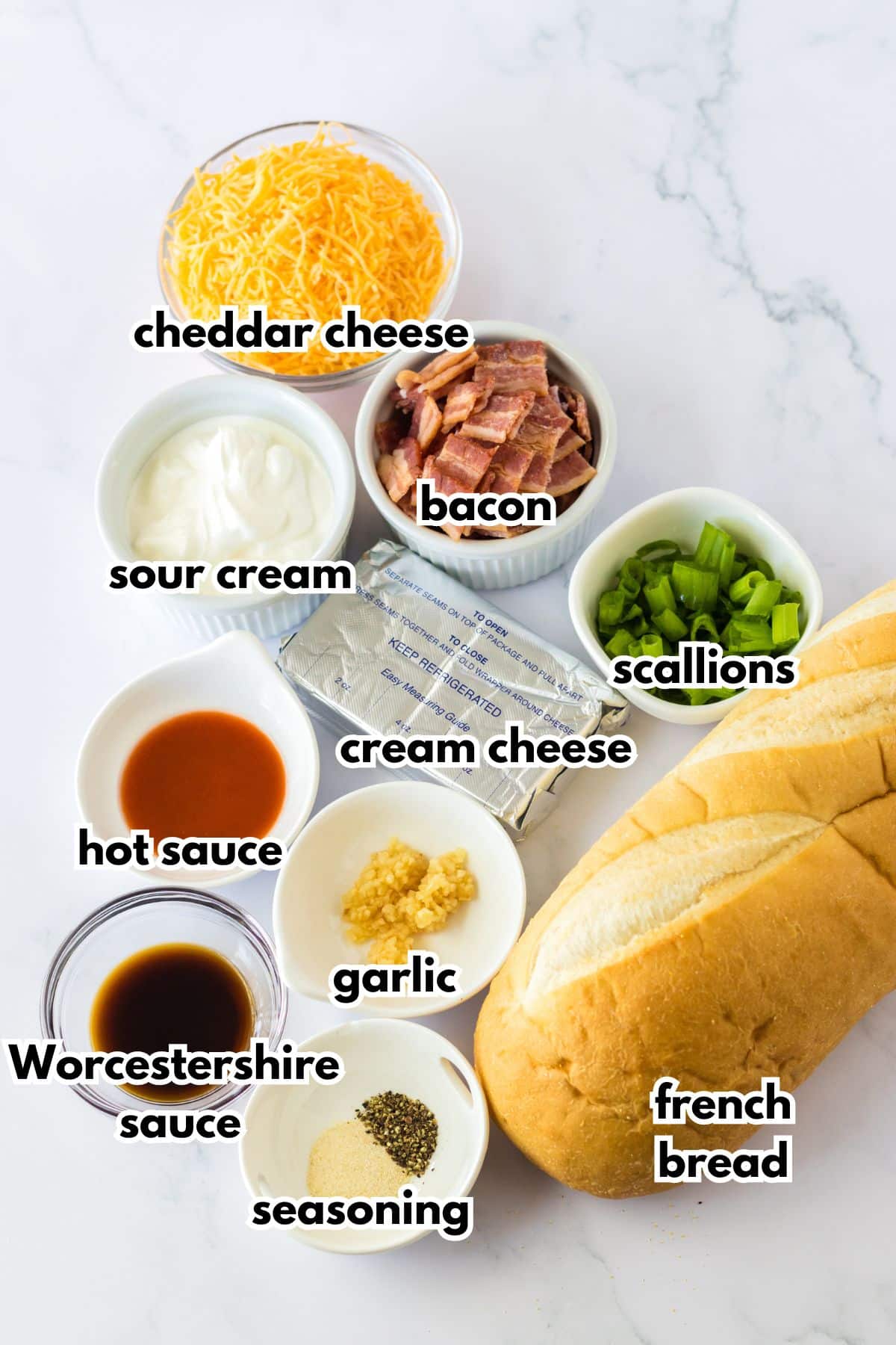 bowls of cheddar cheese, sour cream, bacon, scallions, hot sauce, cream cheese, garlic, seasonings, and worcestershire sauce and a loaf of french bread.