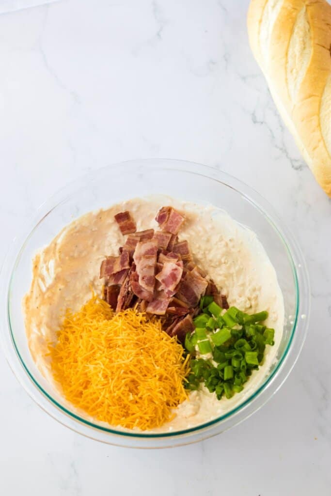 bacon, cheese, and green onions being mixed into cream cheese.