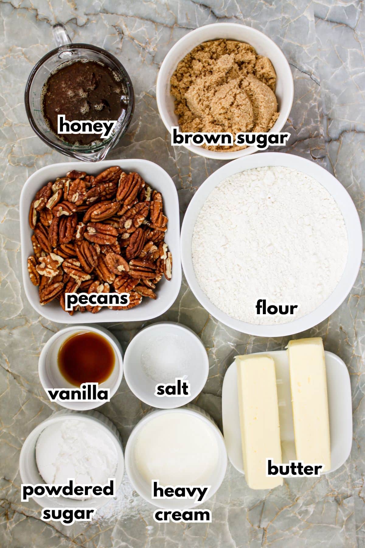 bowls of honey, brown sugar, pecans, flour, vanilla, slat, powdered sugar, heavy cream and butter on a counter.