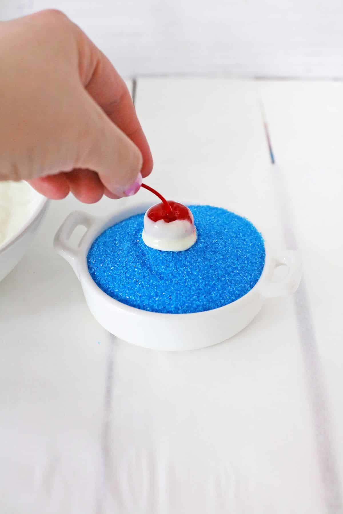 cherry being dipped into blue sprinkles.