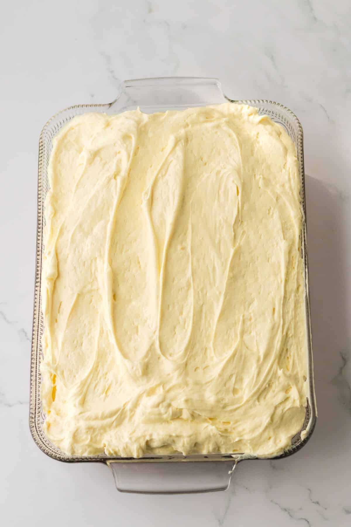 pudding layer being spread on top of a cake in a glass baking dish.