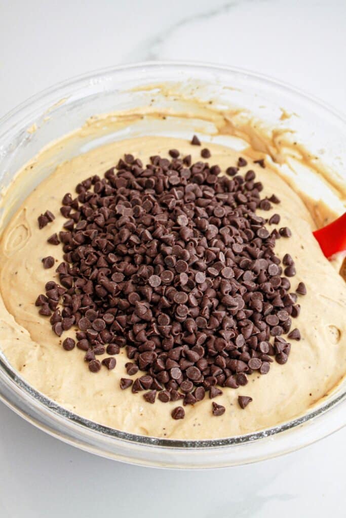 mini chocolate chips being added to the batter in a large glass bowl.