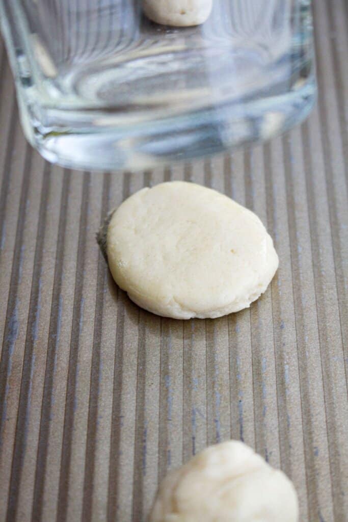 cookie dough being flattened on a cookie sheet.