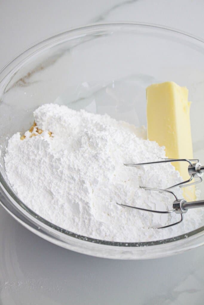 powereded sugar, vanilla, and butter being mixed in a glass mixing bowl.