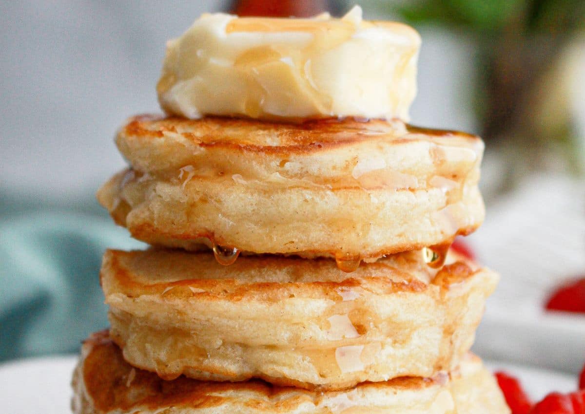 fluffy pancakes stacked on a plate and topped with butter and syrup.