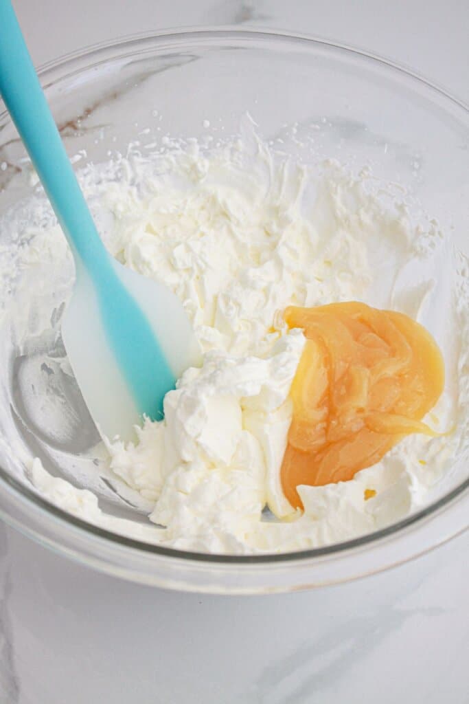 lemon curd being folded into a filling in a glass bowl.