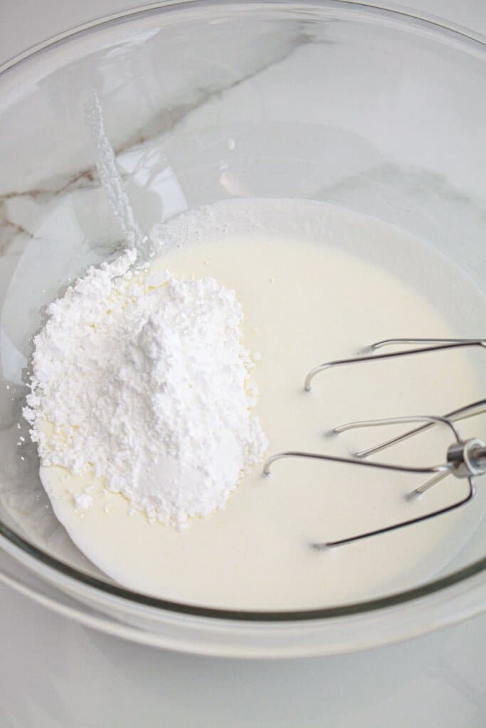 powdered sugar and heavy cream being mixed in a glass bowl.