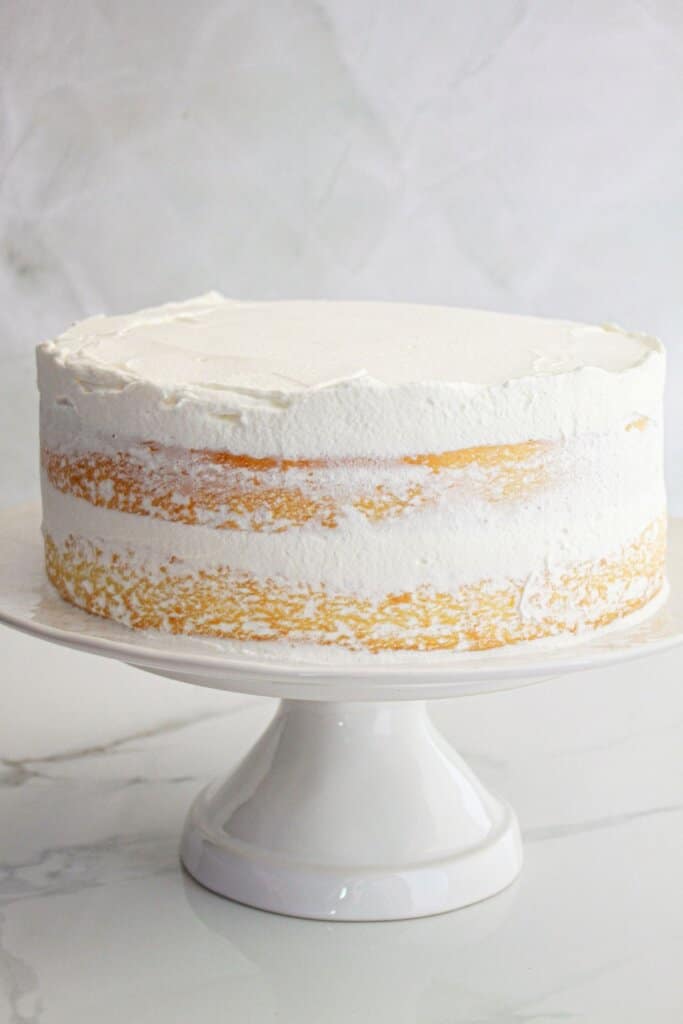 lemon cream cake being frosted on a cake stand.
