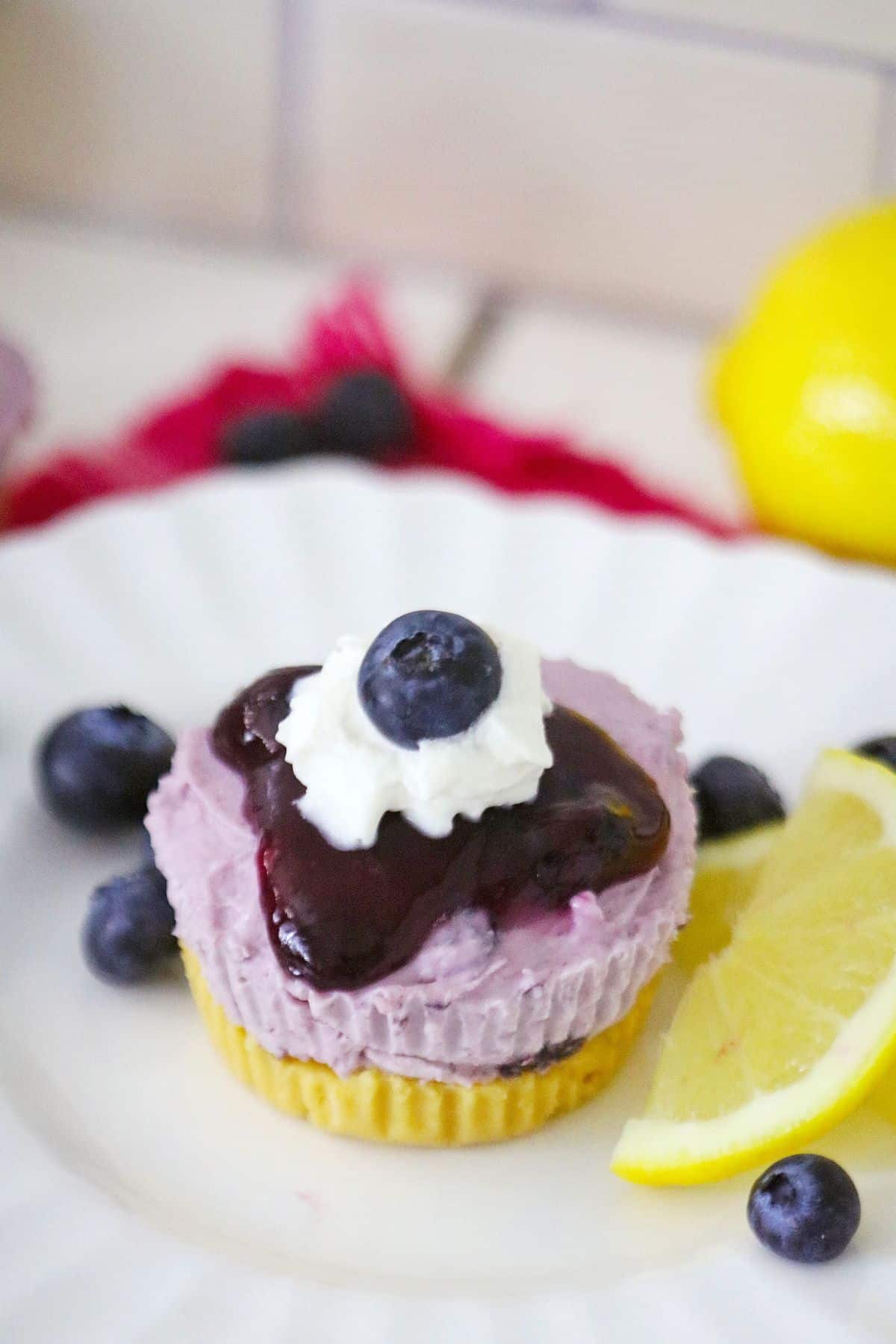 mini blueberry lemon cheesecake on a small plate with lemon slices and fresh blueberries.