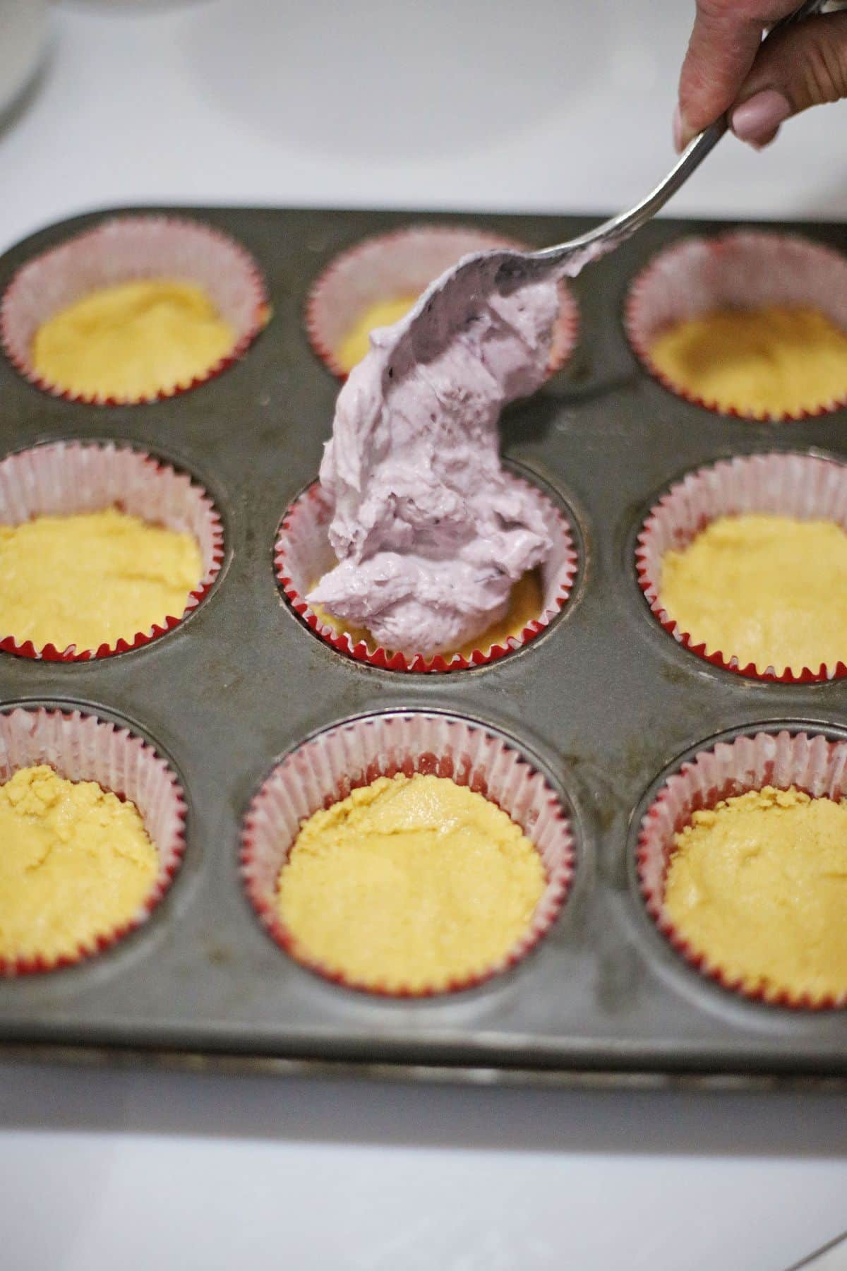 cream cheese filling being added to a muffin pan.