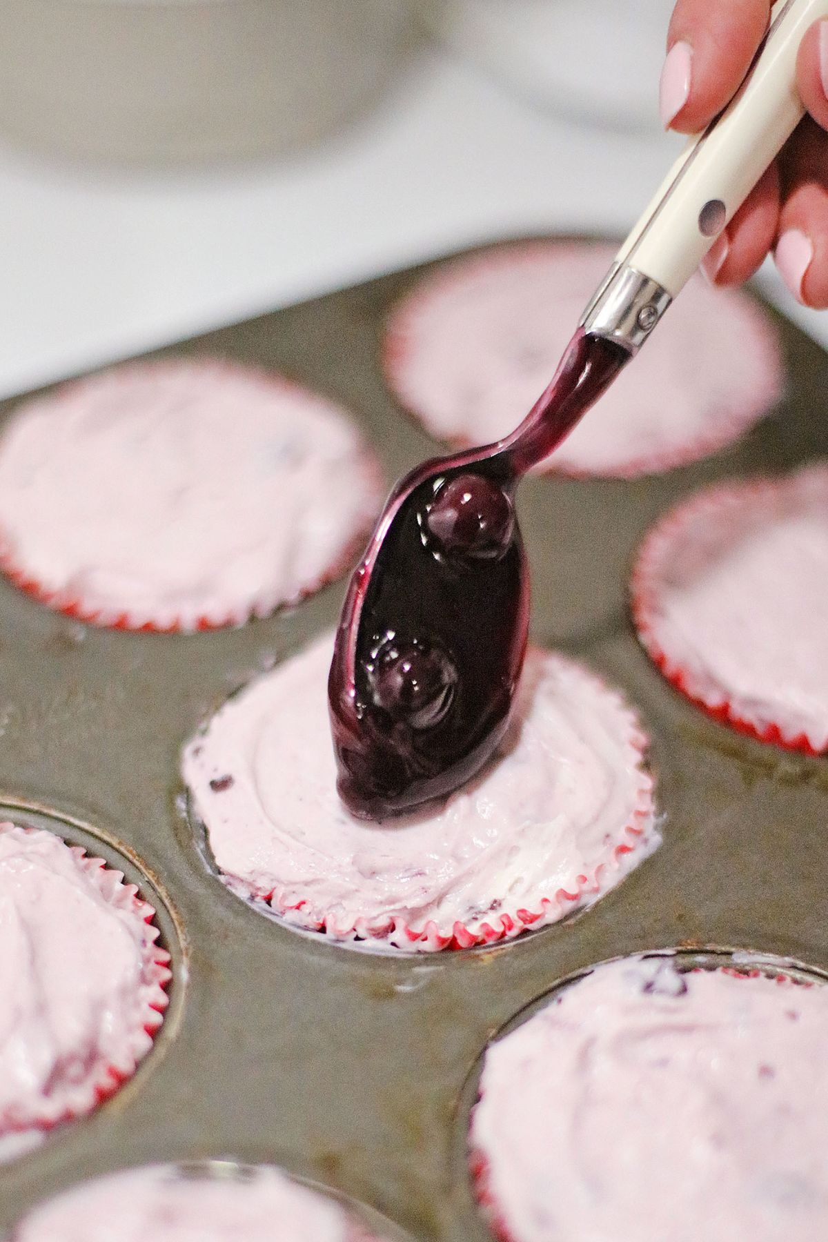 blueberry pie filling being spread on top of cheesecakes.