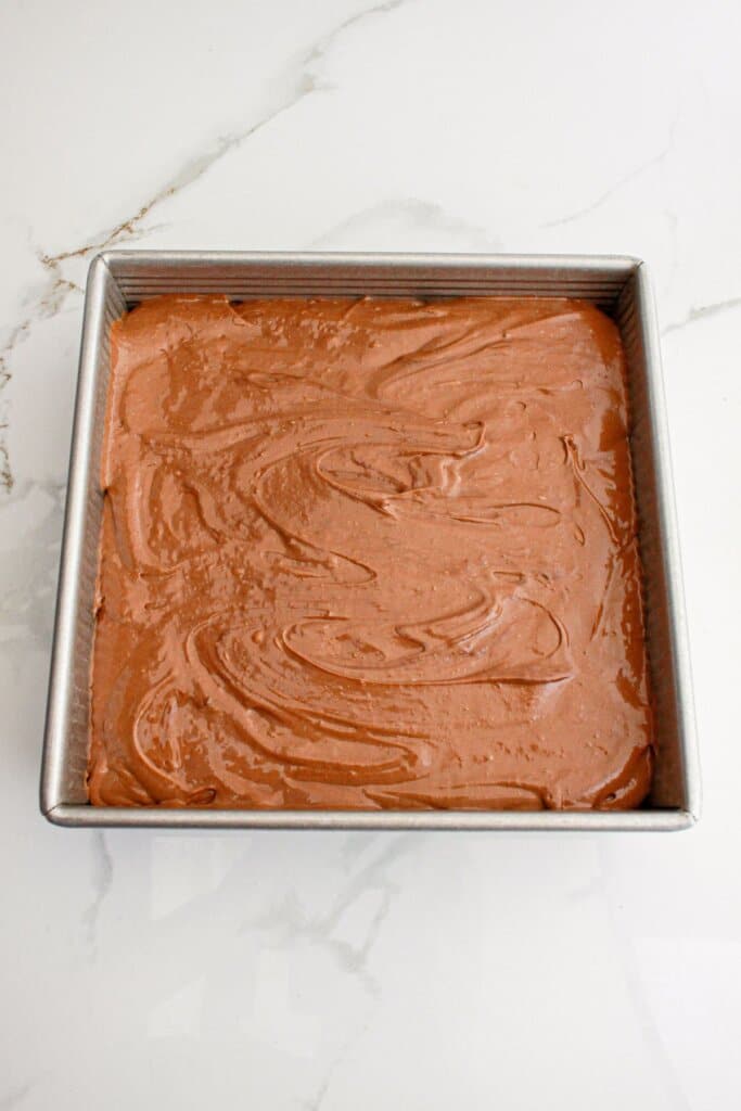 nutella cheesecake bars being spread on top of crust in a baking pan.
