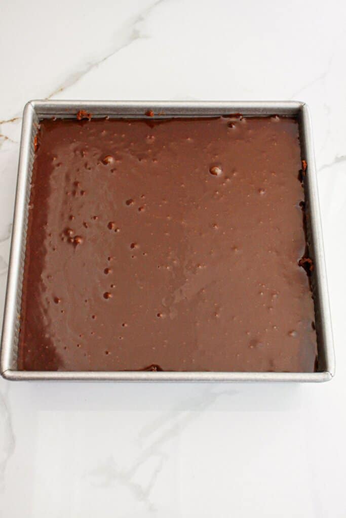 chocolate ganache being poured on top of bars in a baking pan.