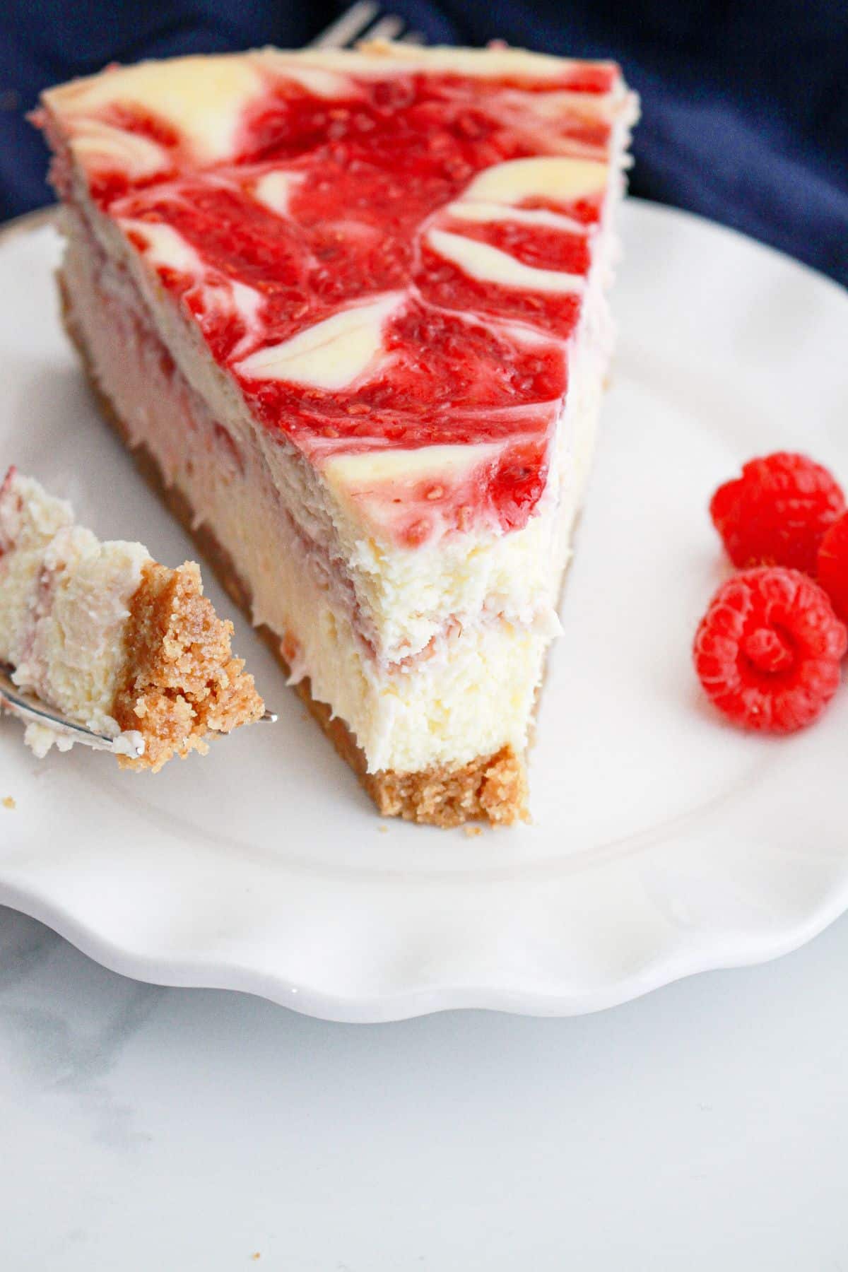 slice of raspberry swirl cheesecake on a plate with a bite missing.