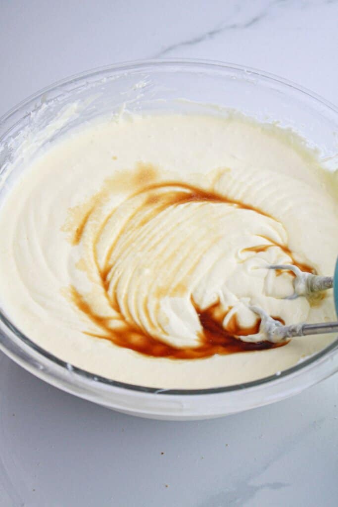 vanilla extract and lemon extract being added to batter in a glass bowl. w