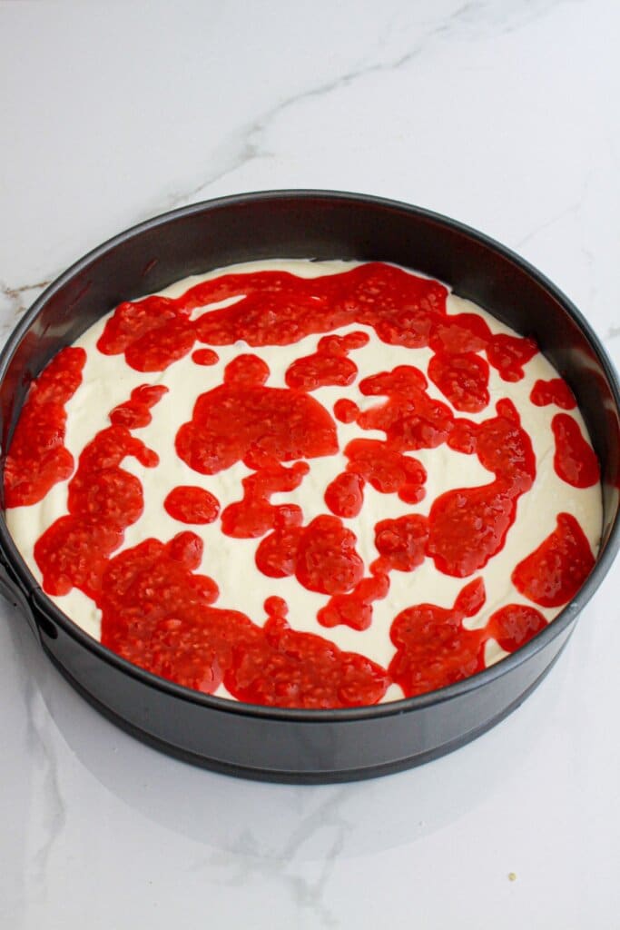 raspberry swirl being added to cheesecake in a springform pan.