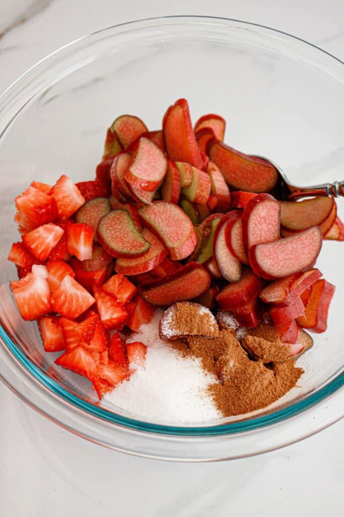 strawberry and rhubarb being coated in a sugar and cinnamon in a glass bowl.