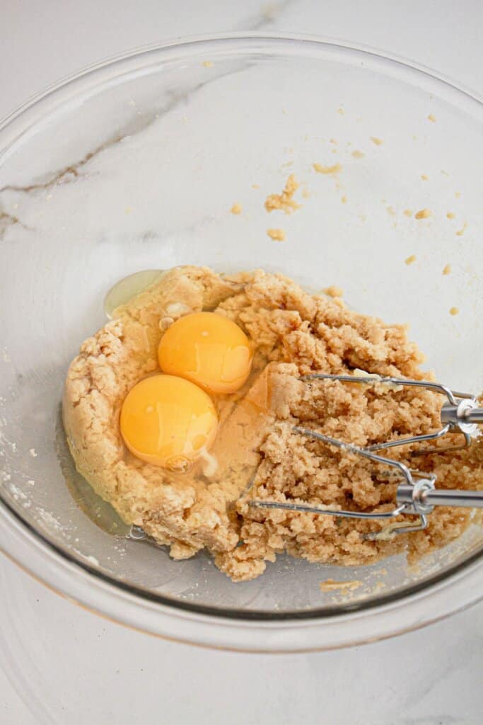 eggs, butter, and brown sugar being mixed togehter in a large glass bowl.