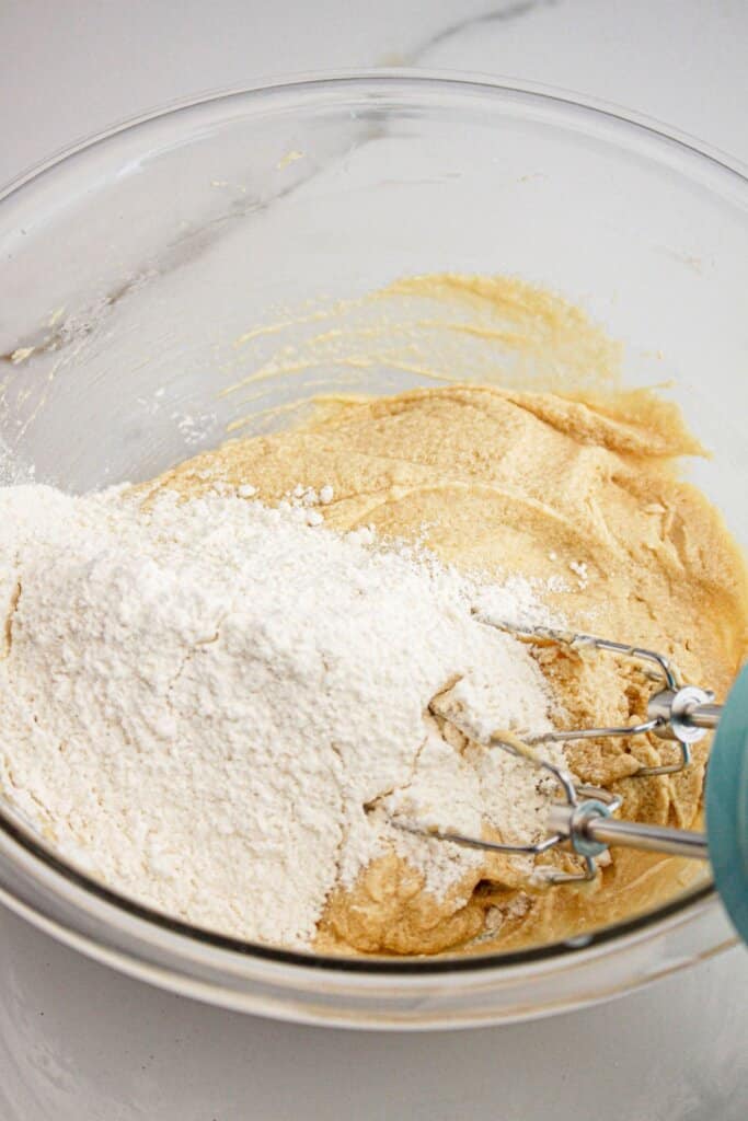 flour being added to wet ingredients in a glass mixing bowl.