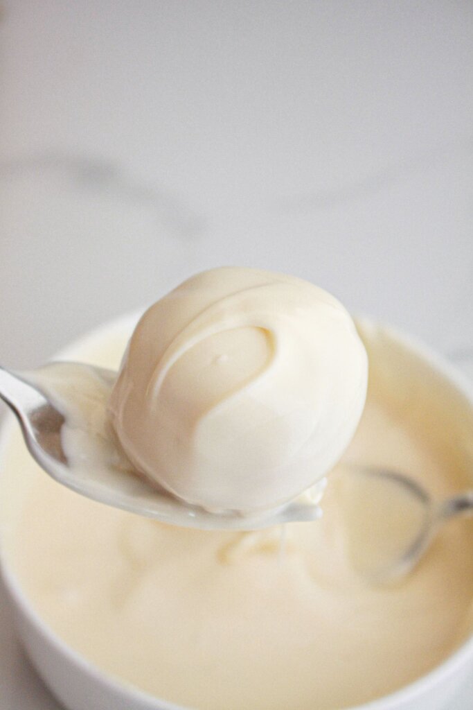 cookie ball being dipped into melted white chocolate.