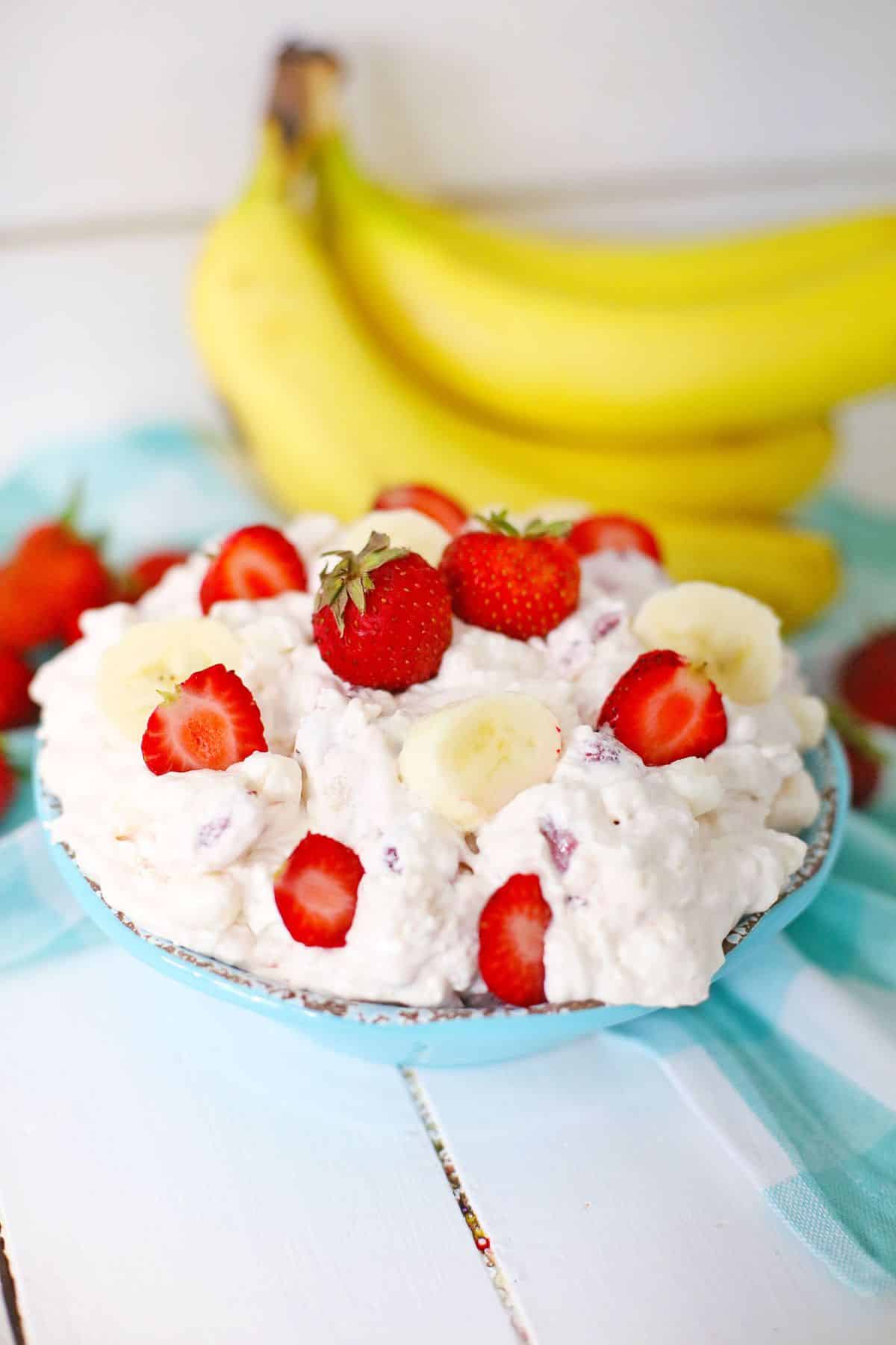 bowl full of strawberry banana cheesecake salad and topped with sliced strawberries.