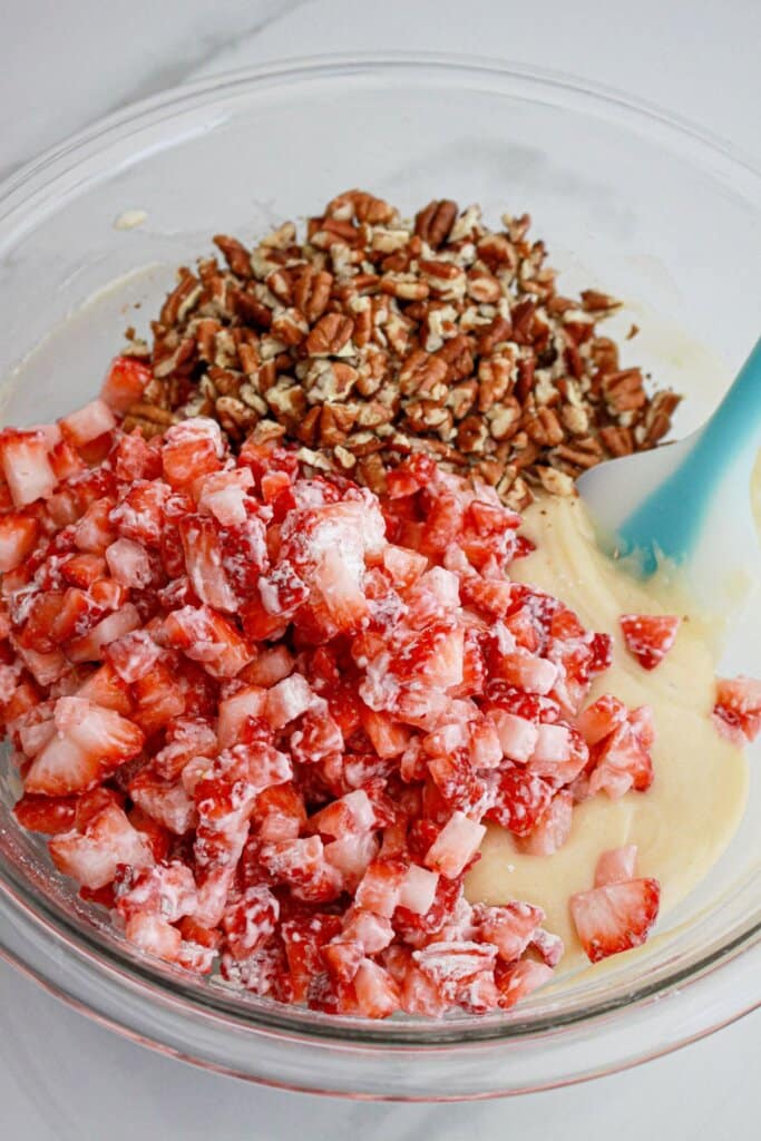 fresh strawberries and chopped pecans being folded into batter in a large glass bowl.