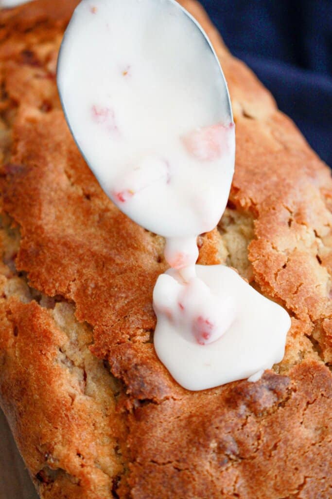 strawberry glaze being poured on top of a loaf cake.