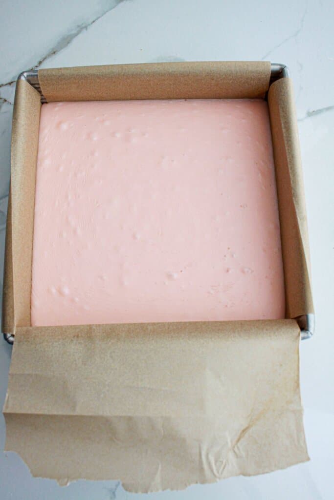 white chocolate raspberry fudge in a parchment lined baking dish.