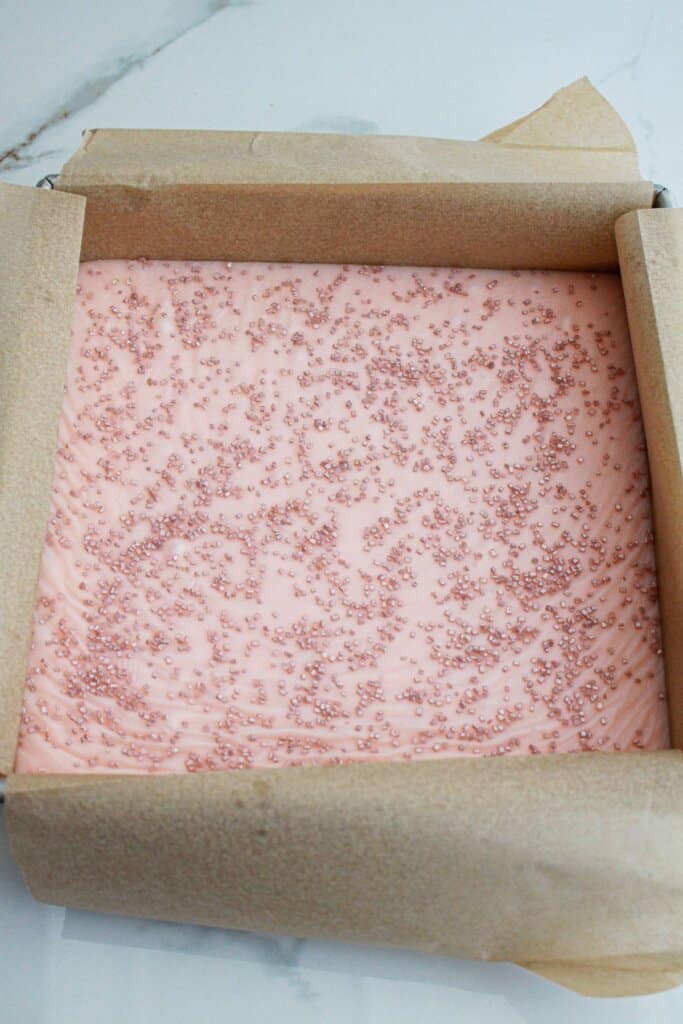 uncut white chocolate raspberry fudge in a parchment lined baking pan.