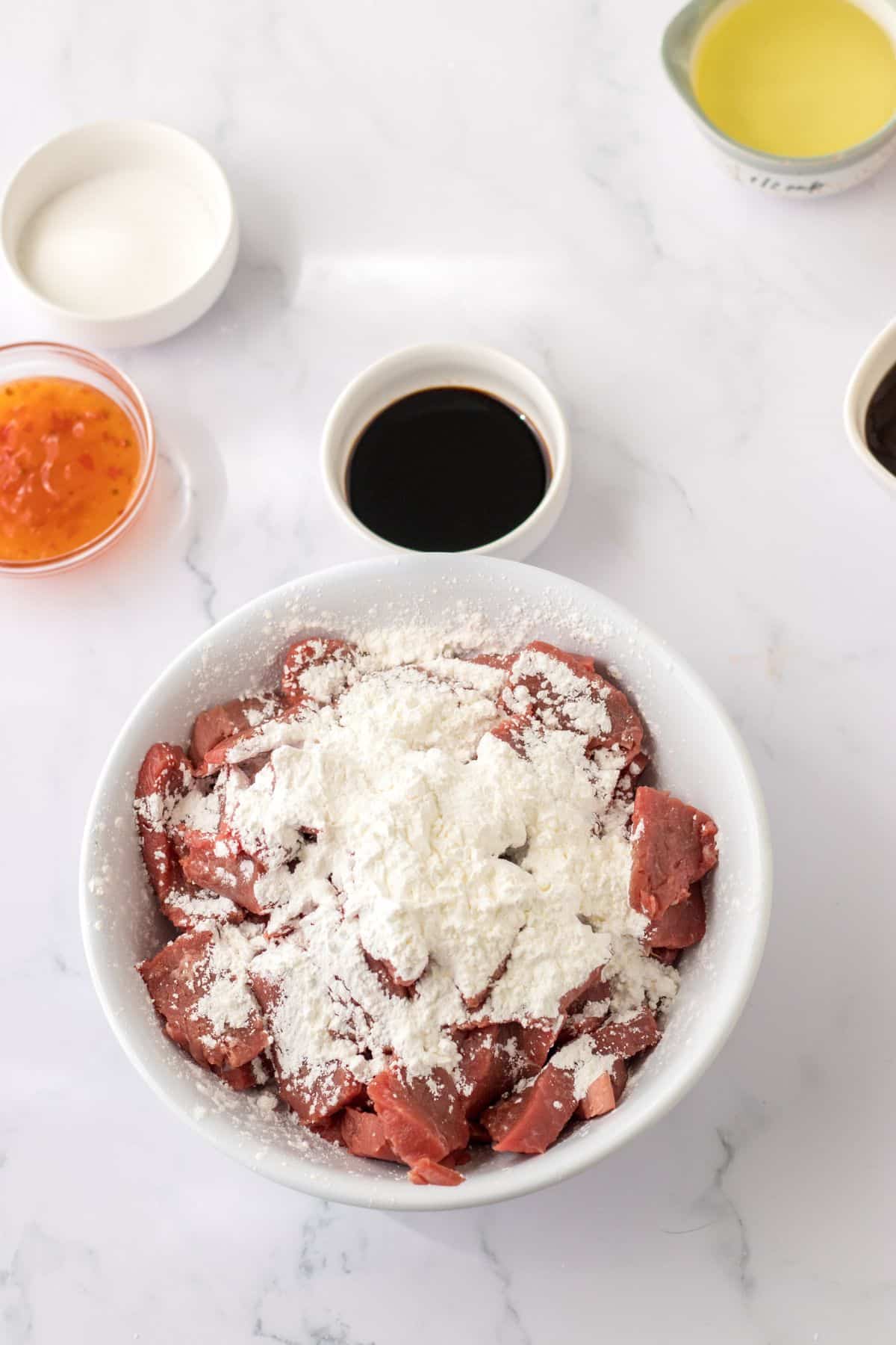 beef being coated cornstarch in a mixing bowl.