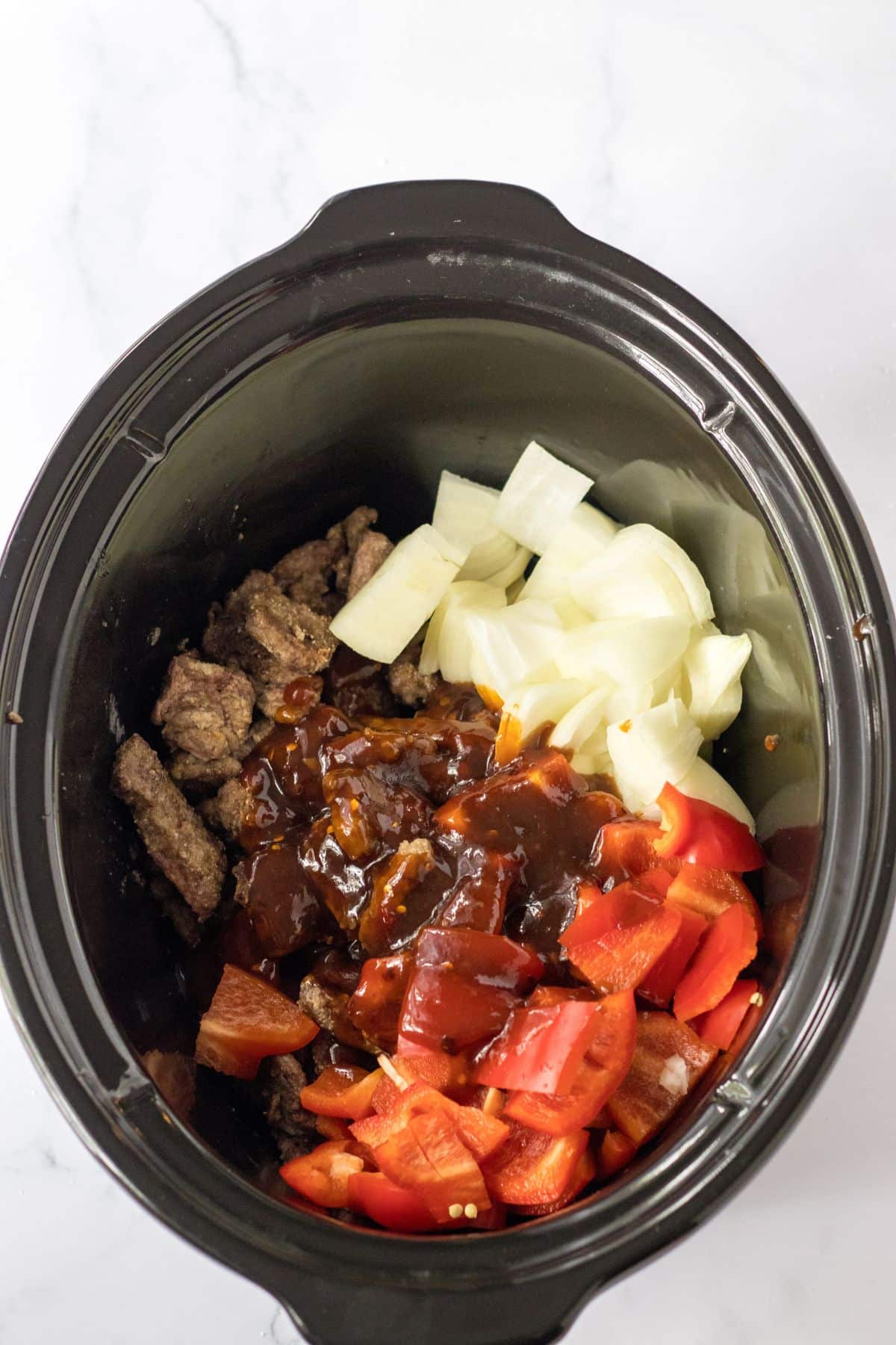 beef, onions, peppers, and sauce in a slow cooker.