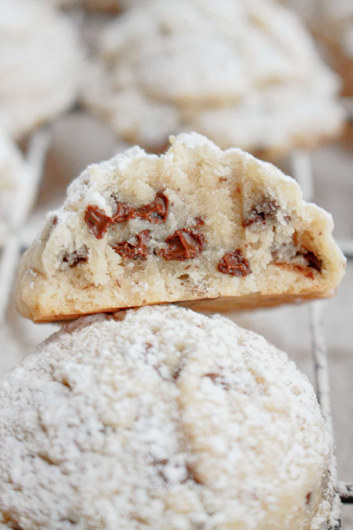two chocolate chip snowball cookies stacked on top of each other with the top one bitten in half.