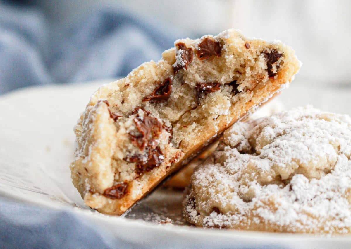 two chocolate chip snowball cookies on a plate with one bitten in half.