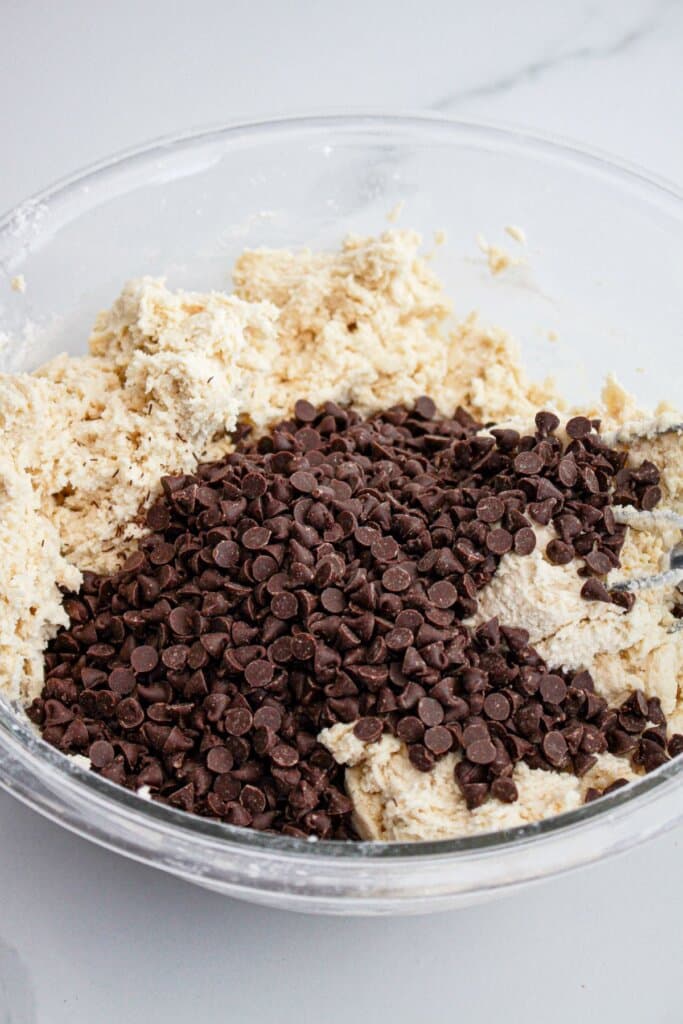 chocolate chips being folded into cookie dough in a mixing bowl.