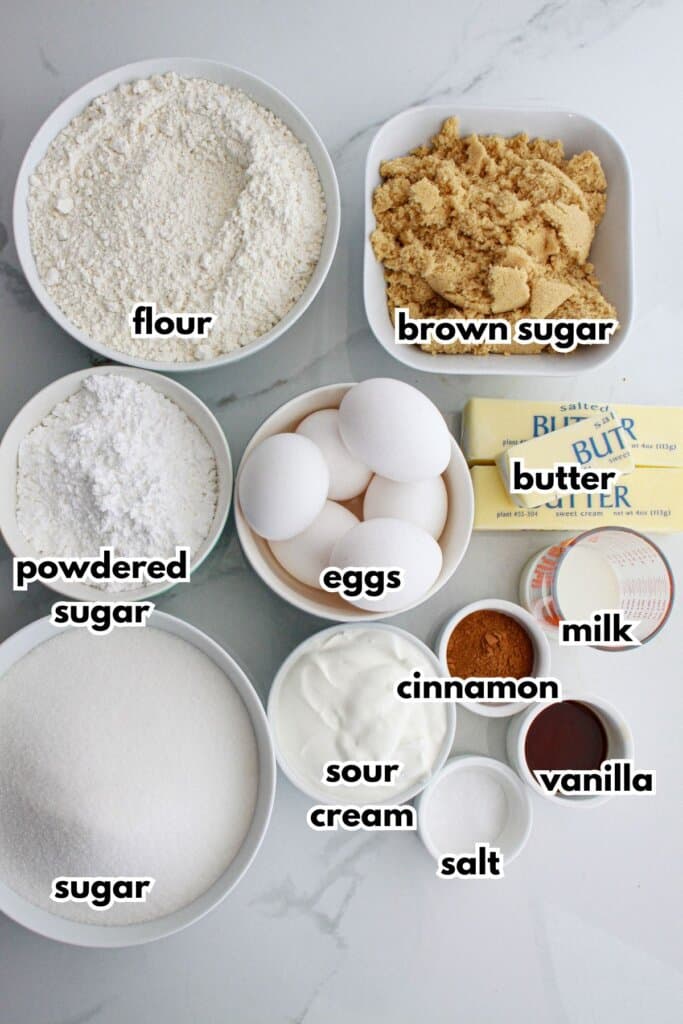 flour, brown sugar, powdered sugar, eggs, butter, sugar, sour cream, salt, cinnamon, vanilla, milk on a counter.