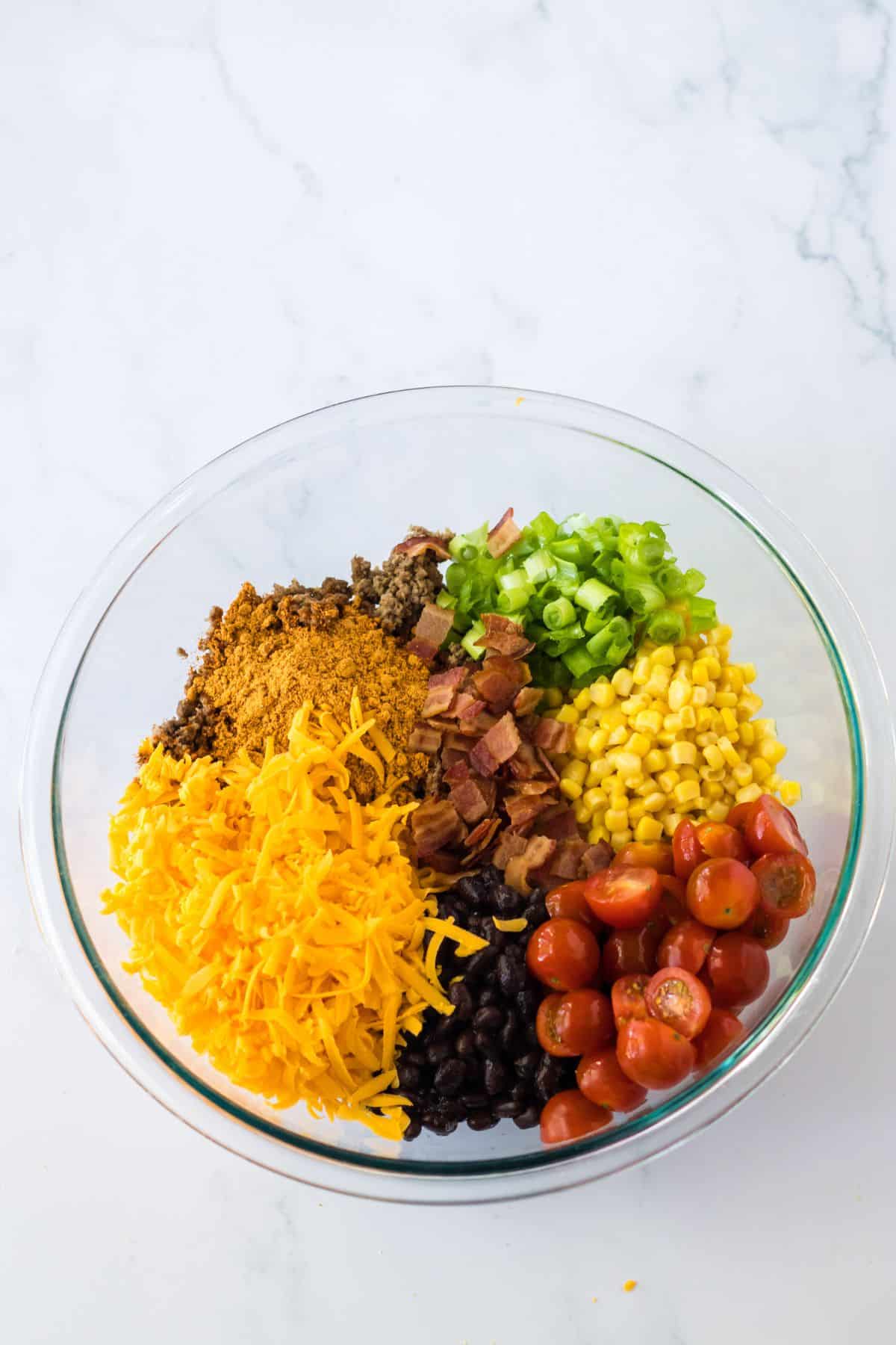 tomatoes, seasonings, corn, beans, and cheese, being added to a large mixing bowl.