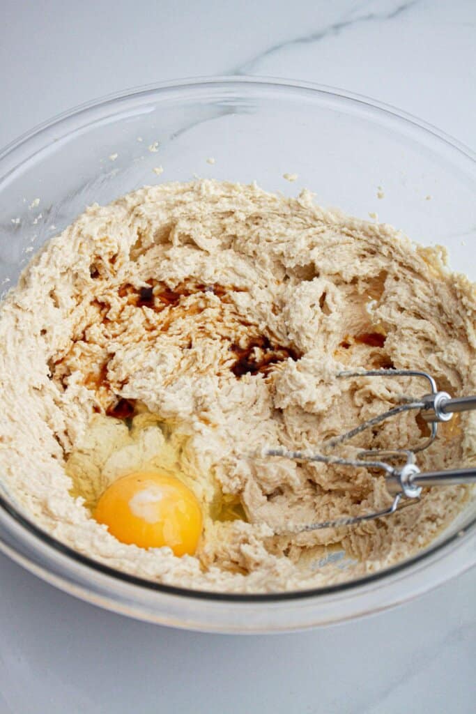eggs and vanilla extract being added to dough in a glass mixing bowl.