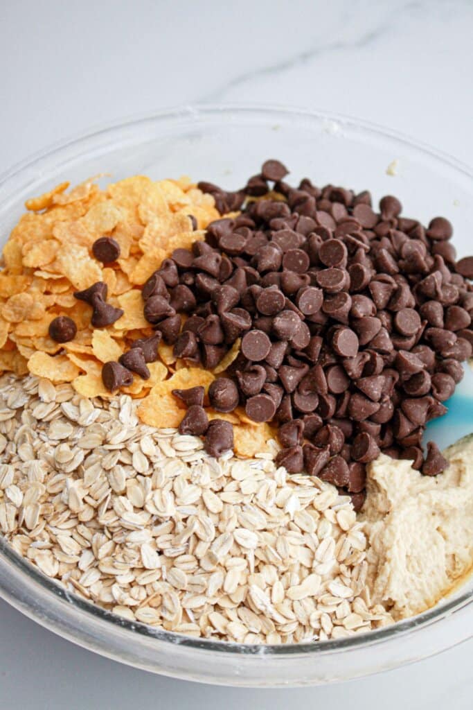 oatmeal, cornflakes, and chocolate chips being stirred into cookie dough.
