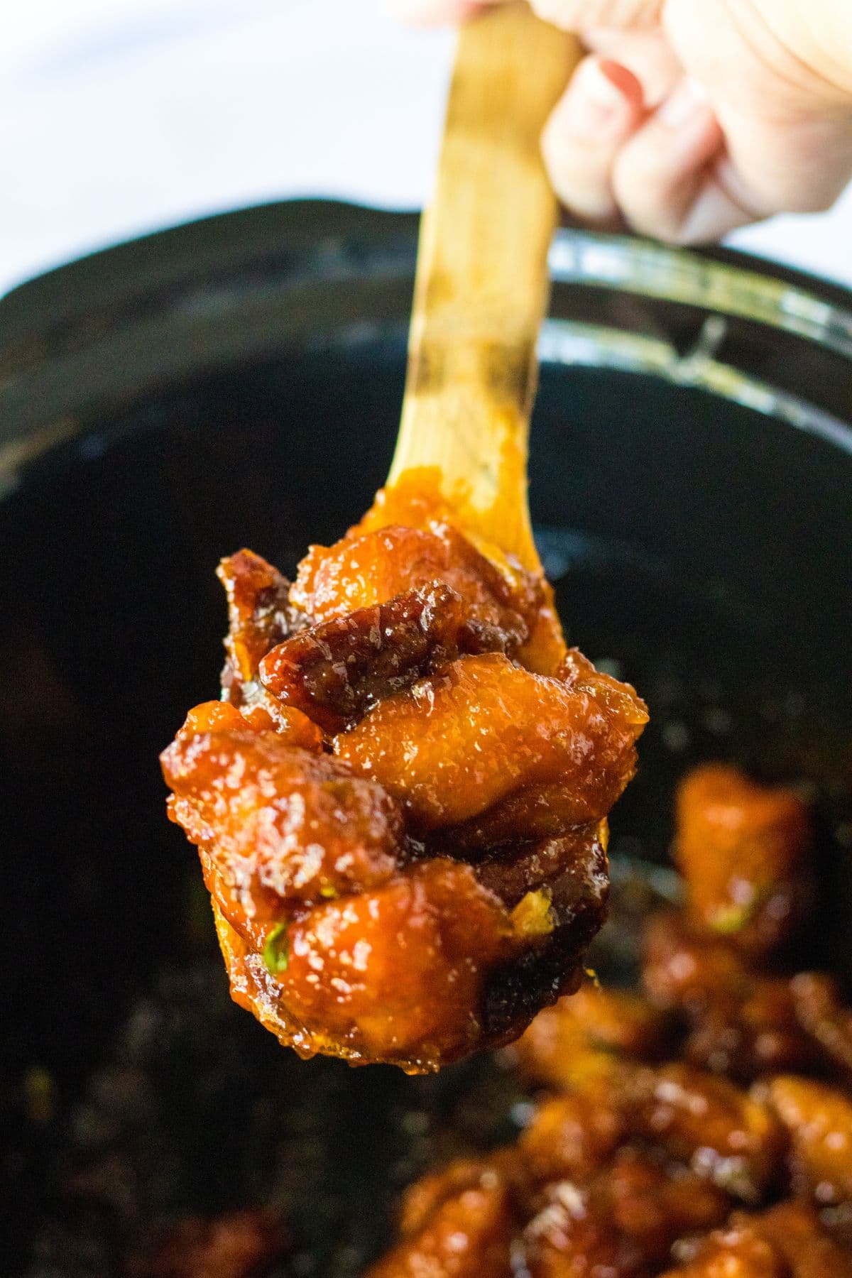 wooden spoonful of firecracker chicken held above a slow cooker.