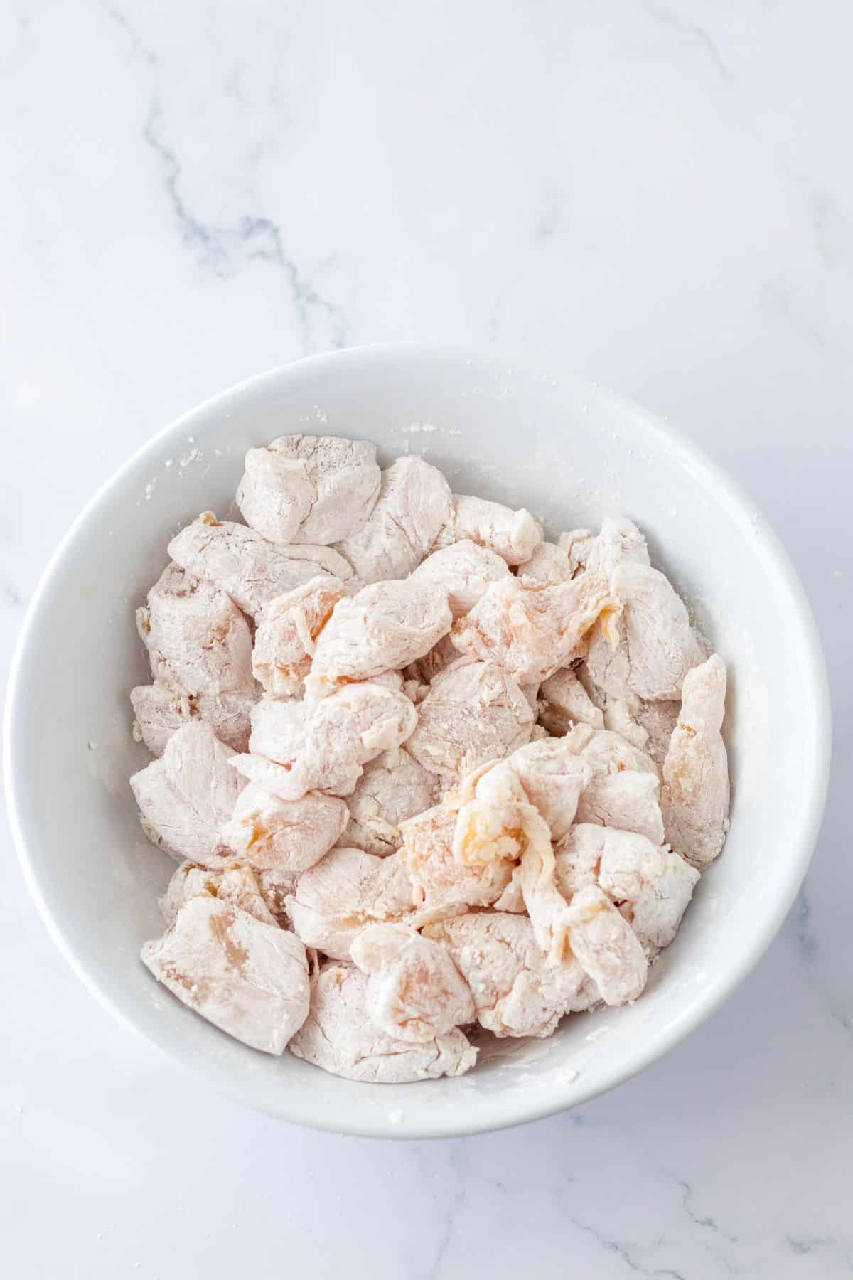 chicken breast pieces being coated in cornstarch.