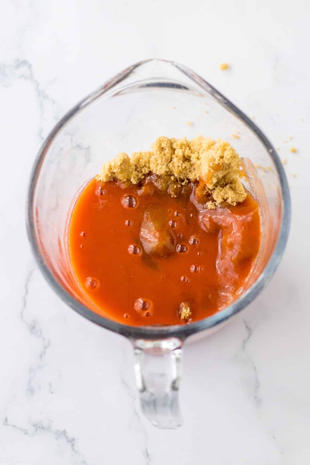 buffalo sauce and brown sugar being mixed in a measuring cup.