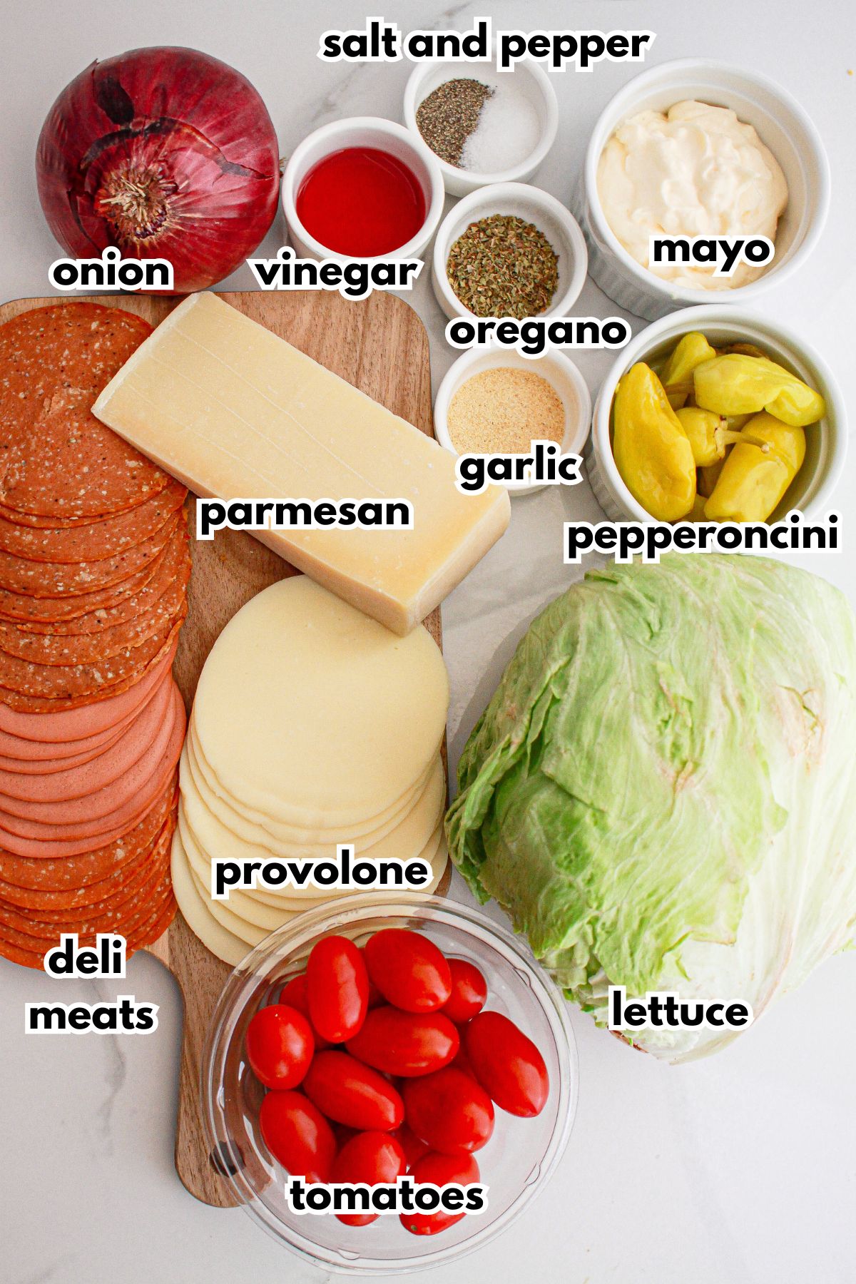 bowls of red onion, deli meat, provolone, parmesan cheese, vinegar, salt, pepper, oregano, garlic, mayo, pepperoncini, lettuce, and tomatoes.